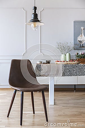 Brown chair under lamp in white dining room interior with table and wall with molding. Real photo Stock Photo