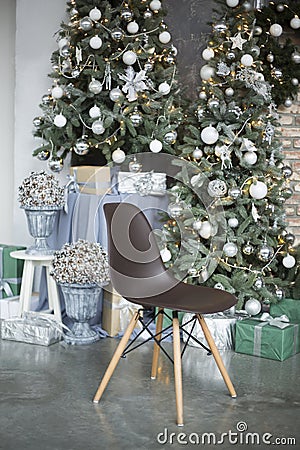 The brown chair on wooden legs costs in studio against the background of the decorated green Christmas tree cones in a vase Stock Photo