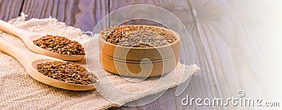 Brown flax seeds or flax seed in a small bowl on sacking and two wooden false on a brown wooden table Stock Photo