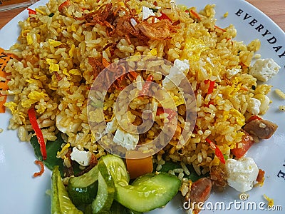 Brown fried rice with with chili,cucumber and fried onion in the white plate on the wooden table. Top view close up details. Stock Photo