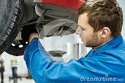 Competent mechanic in blue uniform examining car suspension Stock Photo