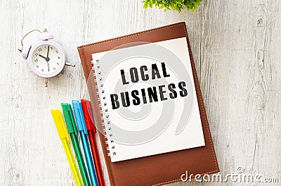 Brown notepad, inscription LOCAL BUSINESS, colored pens, clock on a wooden background. Business concept Stock Photo