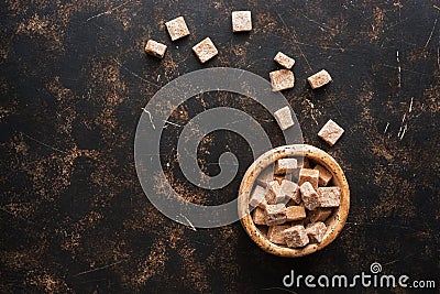 Brown sugar cubes in a bowl on a dark background. Top view, space for your text Stock Photo