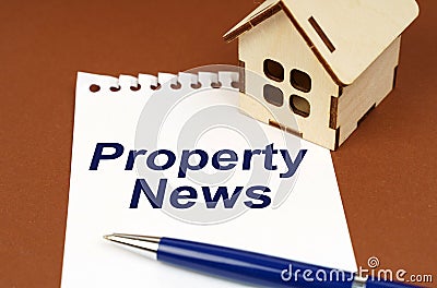 On a brown surface is a house, a pen and a notepad with the inscription - Property News Stock Photo