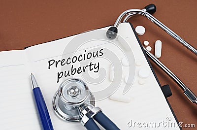 On a brown surface lie pills, a pen, a stethoscope and a notebook with the inscription - Precocious puberty Stock Photo