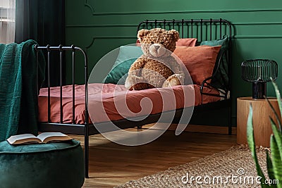 Brown teddy bear on single metal bed with burn orange and emerald green bedding Stock Photo