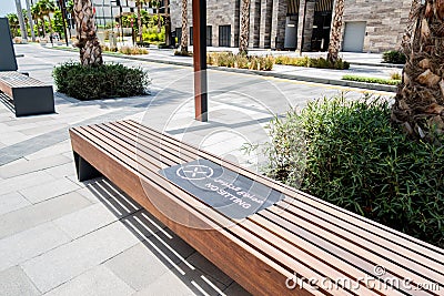 Brown wooden bench forbidden to sit with NO SITTING sign in arabic and english, safety precautions due to coronavirus in Dubai. Editorial Stock Photo