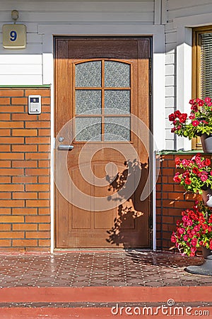 A brown wooden door in a brick wall in the courtyard of a house with a pavement and a bed of flowers. Landscape design Editorial Stock Photo