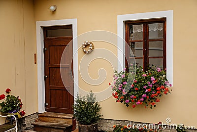 Brown wooden door and vintage window with a red and pink flowers in a pot on a beige wall. Typical beautiful streets of the Editorial Stock Photo