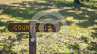 Brown wooden sign in grassy field with courteous written on it Stock Photo