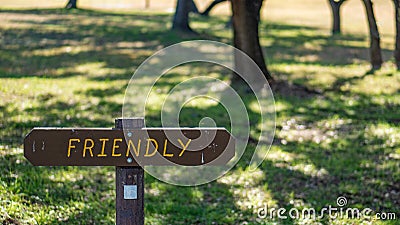 Brown wooden sign in grassy field with friendly written on it Stock Photo