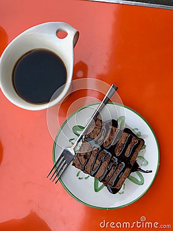 Brownie with Coffee served with Chocolate Sauce at Cafe Shop on Orange Surface. Stock Photo