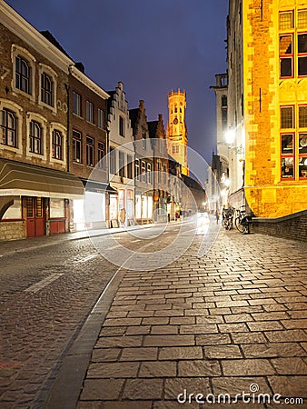Bruges by night. Cobbled street and illuminated historical city centre with Belfort Tower, Belgium, Europe Editorial Stock Photo