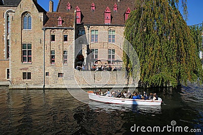 View over water canal with full tourist tour sightseeing boat on medieval house with outside restaurant terrace and green tree Editorial Stock Photo