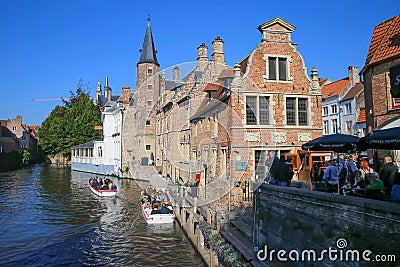 View on pier for tourist water canal boats with outside cafe terrace, medieval brick buildings against clear blue sky Editorial Stock Photo