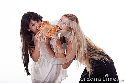 A brunette and blonde with long hair bite a bun in the shape of a heart. Stock Photo