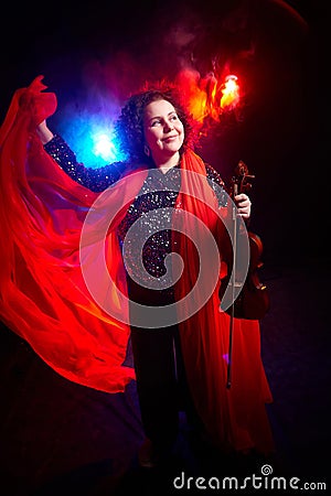 A brunette curly girl in black shiny clothes and with violin on a black background. Model, actress and violinist posing in the Stock Photo