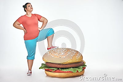 Brunette, funny, plump woman put her leg to a huge sandwich Stock Photo