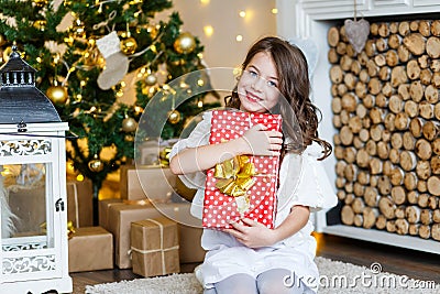 A brunette gilr in front of fur-tree and fireplace with candles and gifts. A girl dreaming. New year`s eve. Christmas Stock Photo