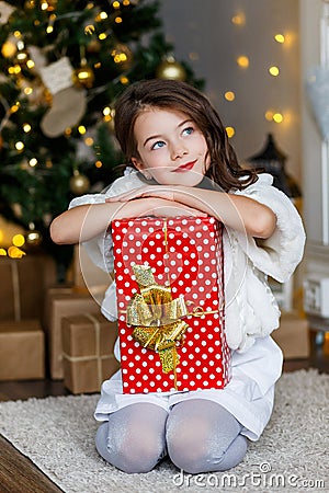 A brunette gilr in front of fur-tree and fireplace with candles and gifts. A girl dreaming. New year`s eve. Christmas Stock Photo