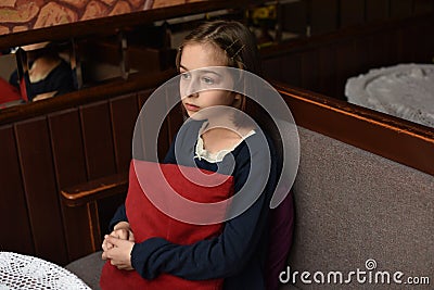 Scared young woman is watching tv. Brunette girl is sitting on the couch with red pillow Stock Photo