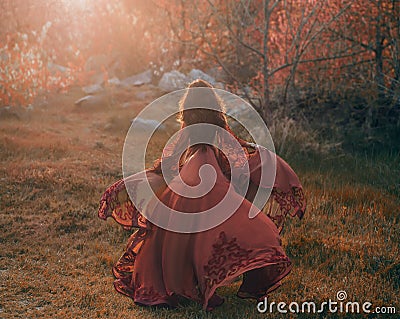 A brunette girl with wavy, thick hair runs to the meeting of the sun. Photo from the back, without a face. The princess Stock Photo