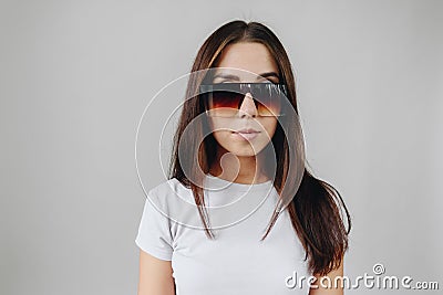 A brunette girl in a white T-shirt on a white background is standing in huge sunglasses Stock Photo