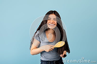 Brunette Indian teen girl brushing her beautiful long hair with natural wooden brush on blue studio background Stock Photo