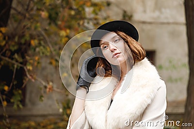 A brunette lady in hat and gloves and coat is standing straightening her hat with her hand. Retro. Outdoors. Stock Photo