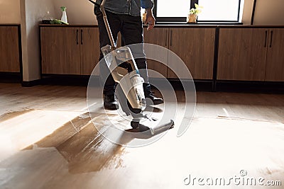 Man vacuuming wooden floor in loft iving room with vacuum cleaner. Close up Stock Photo
