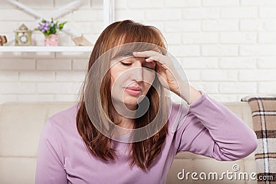 Brunette middle aged woman having headache on home background. Menopause Stock Photo