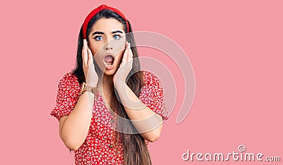 Brunette teenager girl wearing summer dress afraid and shocked, surprise and amazed expression with hands on face Stock Photo