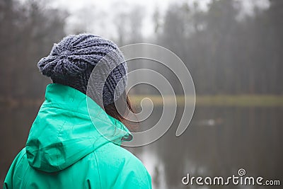 Brunette in winter jacket looking at a small pond near Opava, Czech Republic. Green and blue winter jacket. Lifestyle Stock Photo