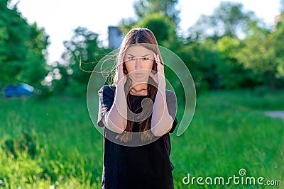 A brunette woman is Asian. Holds his hands near the head. Emotions are a strong headache migraine. In the summer in the Stock Photo