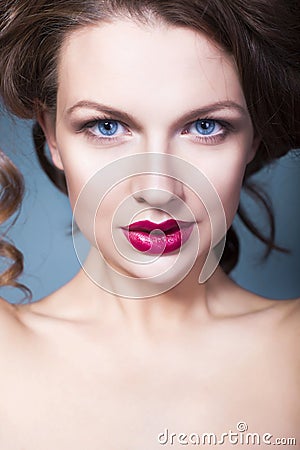 Brunette woman with creative make up violet eye shadows full red lips, blue eyes and curly hair with her hand on her face Stock Photo