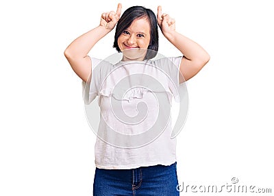 Brunette woman with down syndrome wearing casual white tshirt doing funny gesture with finger over head as bull horns Stock Photo