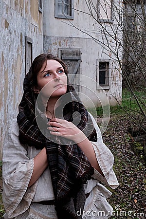 Brunette woman in headscarf and vintage dress on the background of old houses. Girl on the background of a gloomy autumn landscape Stock Photo