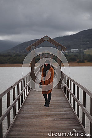 Brunette woman photographer with orange trench coat on a bridge Stock Photo