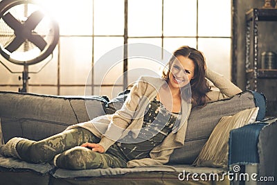 A brunette woman is smiling, relaxing on a sofa Stock Photo