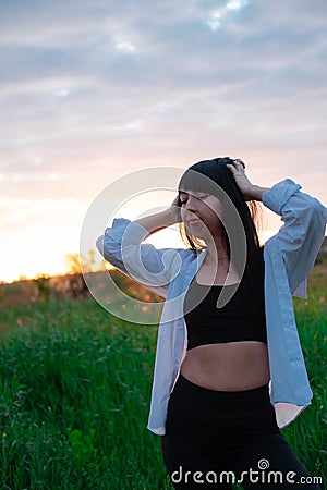 brunette woman in white blouse with baldric on summer field on sunset. peaceful time. millennial generation. calm female Stock Photo