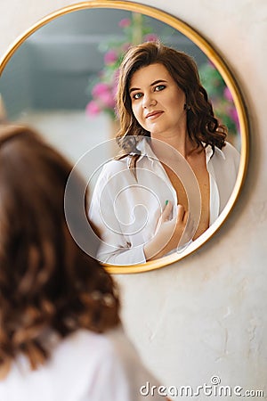 a brunette woman in a white shirt looks at her reflection in a round mirror. Stock Photo