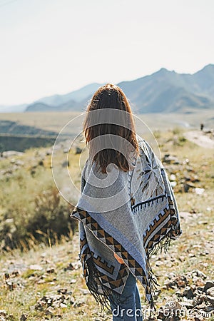 Brunette young woman traveler in poncho from back on road, trip to the mountains, Altai Stock Photo