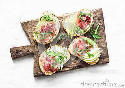 Bruschetta with cream cheese, pear, prosciutto and arugula on wooden chopping board on light background Stock Photo