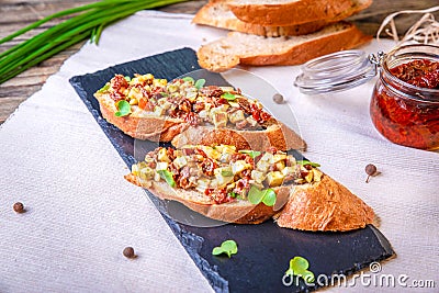 Bruschetta with feta cheese, dried tomatoes, olive oil and fresh microgreen herbs, on a stone plate on a wooden table. Stock Photo