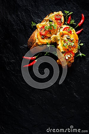 Bruschetta, grilled baguette with addition of tomatoes, cheese and herbs on a black background, top view. Stock Photo