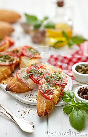 Bruschetta, grilled slices of baguette with mozzarella cheese, tomatoes, garlic and aromatic basil on a white wooden table Stock Photo