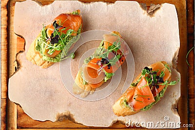 Bruschetta with salmon on wood top view. Smoked salmon toast with guacamole and microgreen Stock Photo