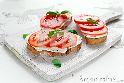 Bruschetta, toast with soft cheese, basil and tomatoes on a white wooden board. Italian healthy snack, food. Stock Photo