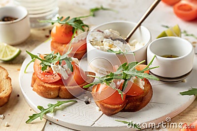 Bruschetta with tomatoes, arugula, olive oil and cheese on white tray on textured background. Fresh italian toasts Stock Photo