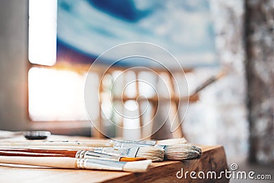 Brushes of the artist close-up on a wooden table in the studio. Background canvas on the easel. Painter workshop Stock Photo